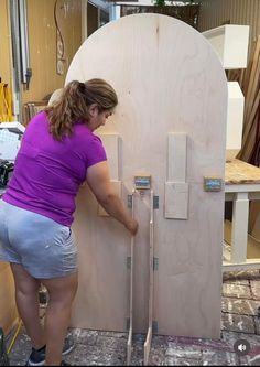 a woman in purple shirt and gray shorts working on a wooden door with two handles