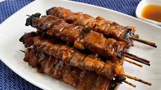 several skewers of meat on a white plate with dipping sauce in the background