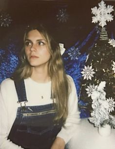 a woman sitting in front of a christmas tree with snowflakes on the background