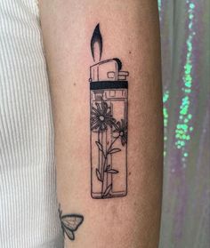 a woman's arm with a small tattoo of a lighter and flowers in it