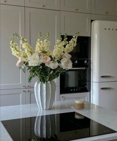 a vase filled with white flowers sitting on top of a counter next to an oven