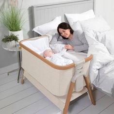 a woman laying in bed next to a baby with a crib on the floor