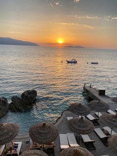 the sun is setting over an ocean with lounge chairs and umbrellas