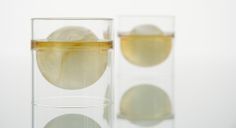 two glasses filled with ice and water on top of a white table next to each other