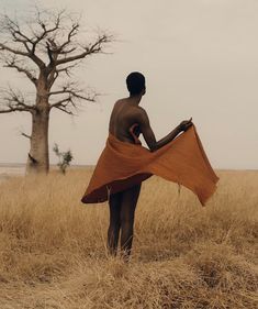 a man standing in the middle of a field holding an orange cloth over his body