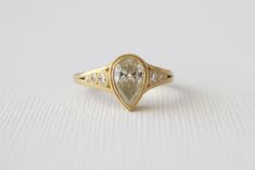 a yellow gold ring with a pear shaped diamond set in the center, on a white background