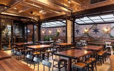 an empty restaurant with wooden tables and chairs, exposed brick walls and glass doors on the ceiling