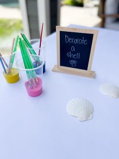 there is a small chalkboard with writing on it next to cups and pencils