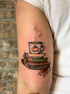 a person with a tattoo on their arm holding a coffee cup and stack of books