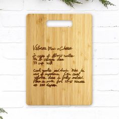 a cutting board with writing on it and pine branches in front of a white brick wall