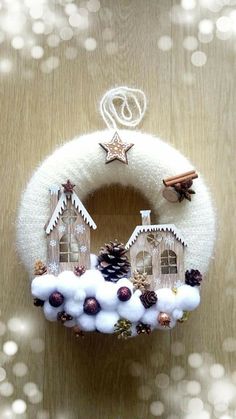 a white wreath with houses and pine cones hanging from it's side on a wooden surface