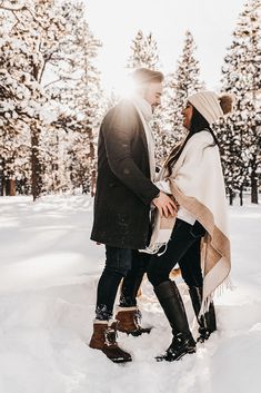 a man and woman standing in the snow holding each other's hands as they look at each other