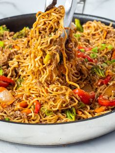 someone is lifting noodles from a skillet with chopsticks into the dish,