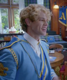 a young man dressed in blue and gold is smiling at the camera while standing next to a table