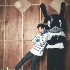 a man standing next to a black rabbit mascot on top of a wooden floor with his leg in the air