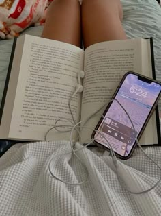 an open book sitting on top of a bed next to a cell phone and headphones