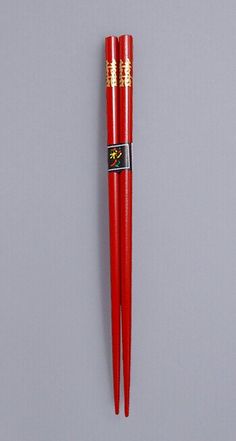 two red chopsticks with gold designs on them sitting next to each other in front of a gray wall