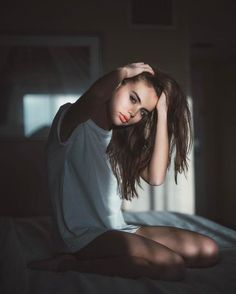 a woman sitting on top of a bed next to a window in a dark room