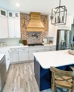 a kitchen with white cabinets and wood flooring next to an island in front of a brick wall