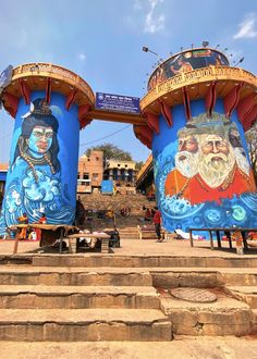 two blue towers with paintings on them in front of some steps and buildings behind them