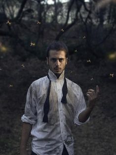 a man in white shirt and black tie standing next to trees with bees flying around him