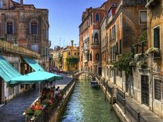 people are sitting at tables on the edge of a canal