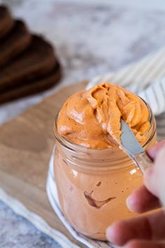 a person is holding a spoon in a glass jar with peanut butter on the side