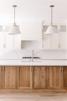 a kitchen with wooden cabinets and white counter tops, two pendant lights over the sink