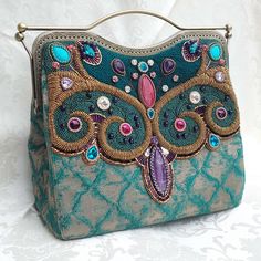 Amethyst-Teal Paradise This One of a kind handbag was created of a brocade material stiffened by vlies, and decorated on one side with rich beadembroidery.  The design has its floral parts, which is highlightended by 3 dimensional beading technique, French wire, Amethyst round beads. In the main part an excellent Amethyst carving gives the design its main character, completed with other carvings (fossil, Turkinite). The crystals give the give the floral design its glamour and extra sparkle.  The Handmade Tapestry Evening Bags, Handmade Tapestry Bags For Evening, Embellished Green Rectangular Shoulder Bag, Green Embellished Rectangular Shoulder Bag, Handmade Turquoise Rectangular Shoulder Bag, Traditional Embellished Green Bag, Traditional Green Embellished Bag, Traditional Green Embellished Bags, Hand Embellished Multicolor Rectangular Bag