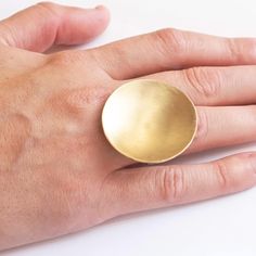 "This is a wonderful Gold colored brass circular dome ring that is simple and clean. Attached to the brass dome is a sterling silver half round band that provides comfort for the fingers. + Dome Material - Brass & Sterling Silver + Dome Size (Diameter) - 1.3125\" (33.3mm) + Dome Depth - 0.25\" (6.3mm) + Ring Material - Sterling Silver + Ring Gauge - 16GA Half Round + Ring Size (US) - 4, 4.5, 5, 5.5, 6, 6.5, 7, 7.5, 8. 8.5, 9, 9.5, 10, 10.5, 11, 11.5, 12, 12.5, 13 + Packaged in a Kraft Box + Gold Minimalist Dome Ring In Brass, Minimalist Gold Dome Ring In Brass, Brass Dome Ring With Polished Finish, Yellow Gold Oval Dome Ring In Brass, Hammered Brass Round Rings, Minimalist Brass Dome Ring For Gift, Oval Brass Dome Ring Gift, Oval Dome Ring In Brass For Gifts, Contemporary Jewelry Rings