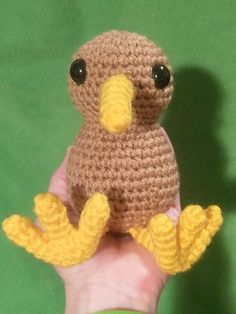 a small crocheted bird sitting on top of a persons hand in front of a green background