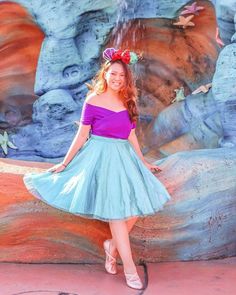 a woman standing in front of a waterfall wearing a blue and purple dress with pink flowers on her head