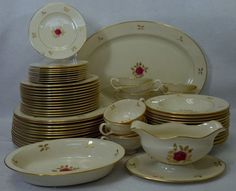 a pile of white and gold china with red flowers on it's rims