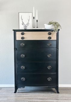 a black dresser with two candles on top and a white vase sitting on top of it