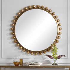 a round mirror sitting on top of a wooden table next to a vase with flowers