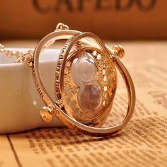 a gold necklace with an hourglass in the middle on top of a table next to a cup