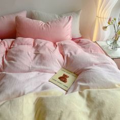 a book is laying on the bed with pink comforter and pillows in front of it