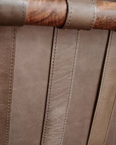 the back of a brown leather chair with wooden slats and stitching on it