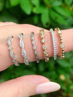 five different types of rings on someone's hand with green plants in the background