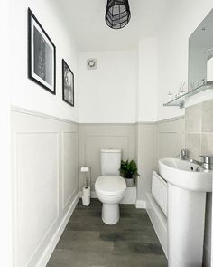 a white toilet sitting in a bathroom next to a sink under a light hanging above it