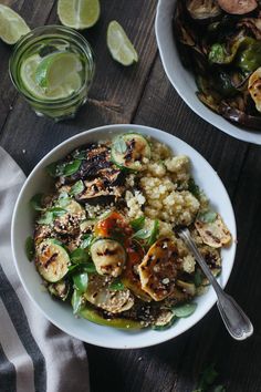 two bowls filled with food on top of a wooden table next to lime wedges