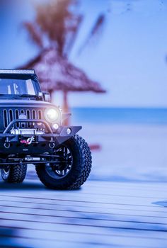 a black jeep is parked in front of an umbrella on the beach with it's lights on