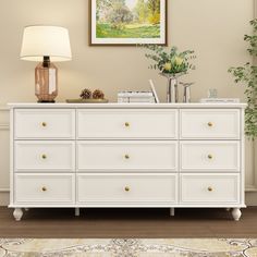 a white dresser sitting in a living room next to a lamp and painting on the wall