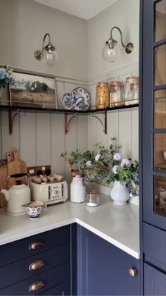 a kitchen with blue cabinets and shelves filled with plates, vases and flowers on the counter