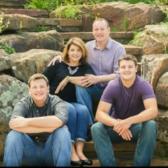 four people are sitting on steps in front of some rocks and trees, posing for a photo