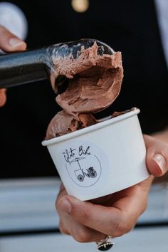 a person is scooping chocolate ice cream out of a paper cup with a spoon