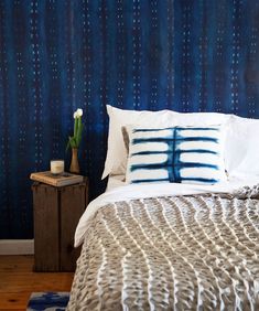 a bed with white and blue pillows on top of it next to a wooden night stand