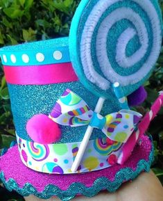 a hand holding up a blue and pink hat with a candy lollipop on it