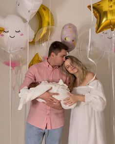 a man and woman holding a baby in front of balloons