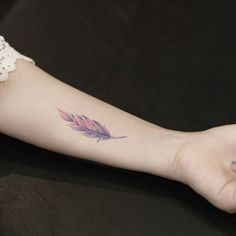 a woman's arm with a tattoo that has a pink feather on the wrist